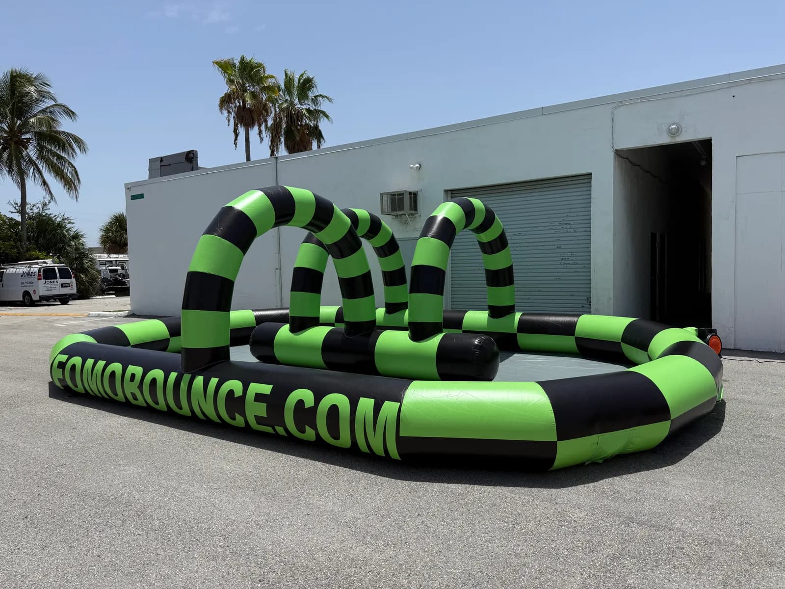 FOMO Bounce inflatable bumper car arena with green and black arches, set up and inflated on a paved lot in Boca Raton