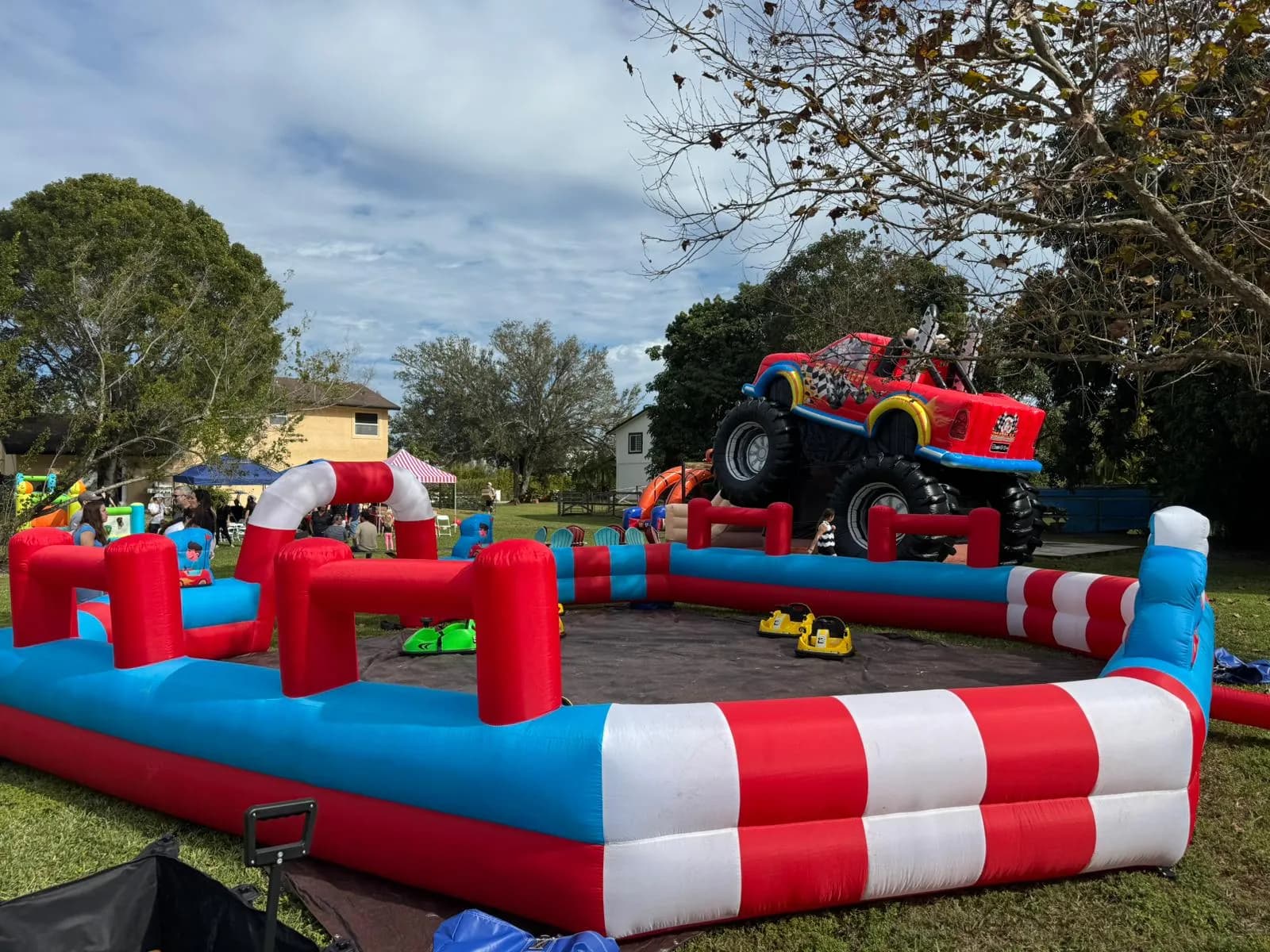Red, white and blue inflatable bumper car track set up on a lawn at a backyard party alongside a monster truck bounce house