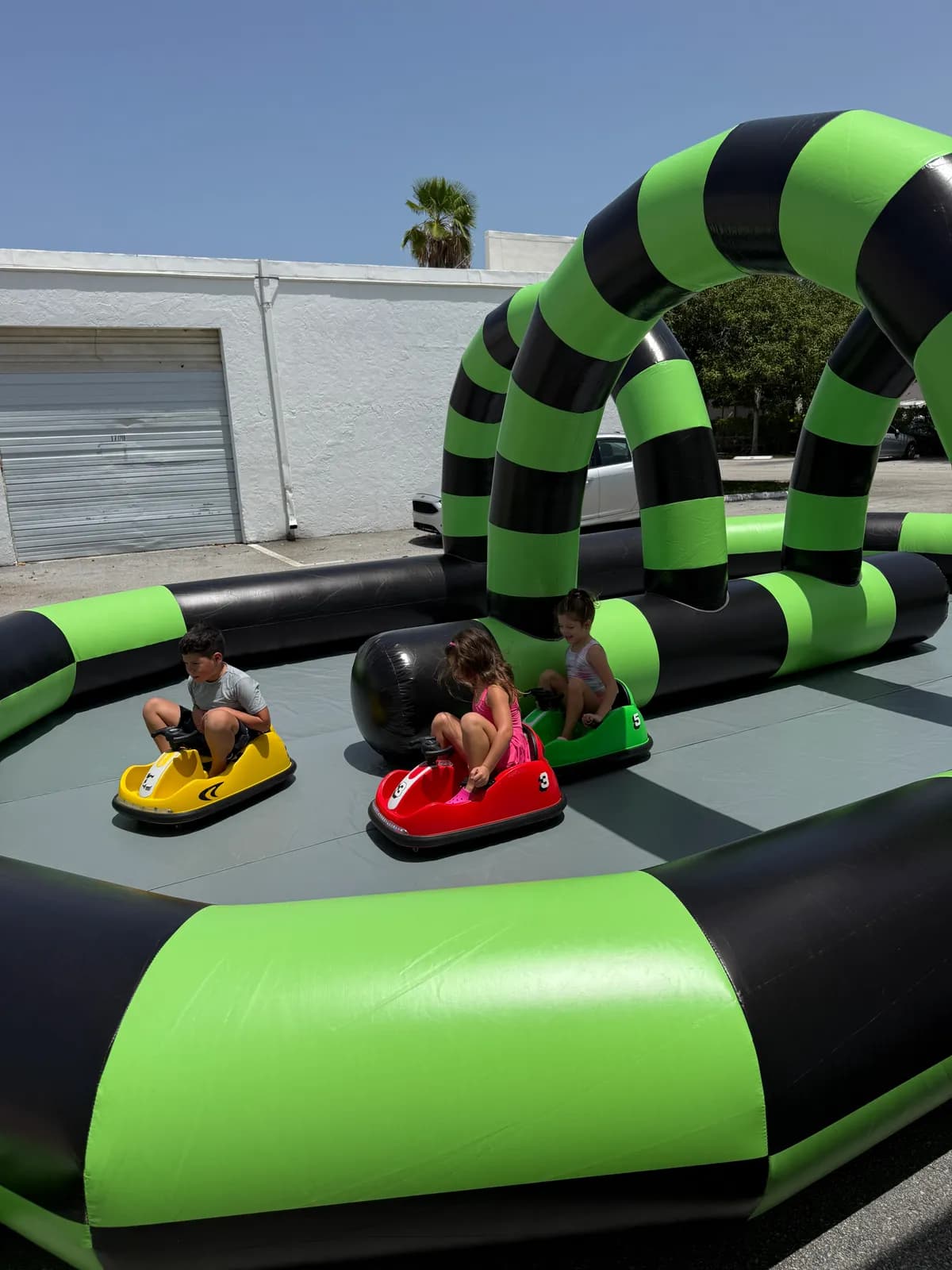 Children driving electric bumper cars inside the soft-walled inflatable arena with overhead racing arches