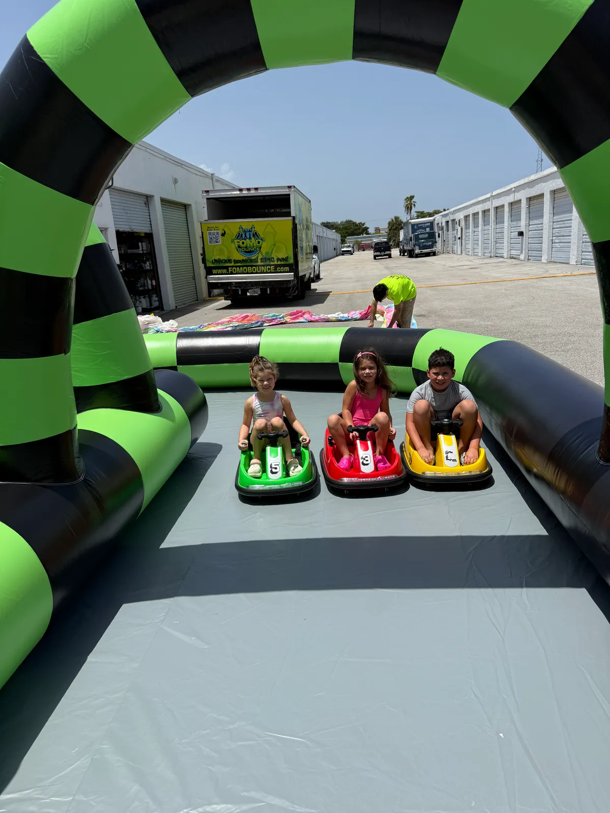 Three children racing yellow, red and green electric bumper cars inside the padded inflatable arena with a staff attendant supervising